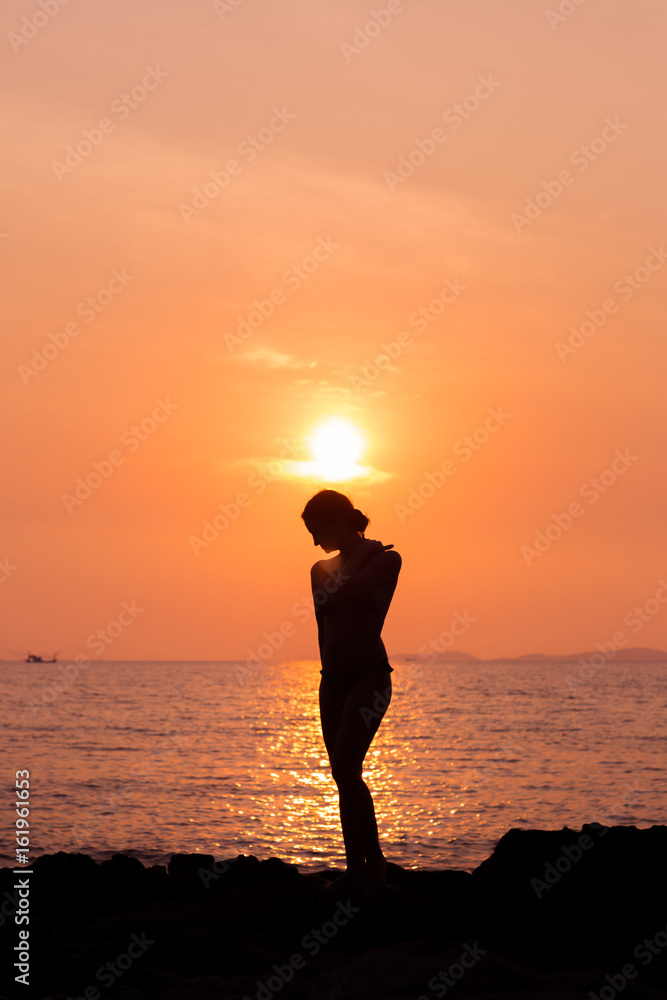 Standing woman silhouette on sunset sea background, back lit