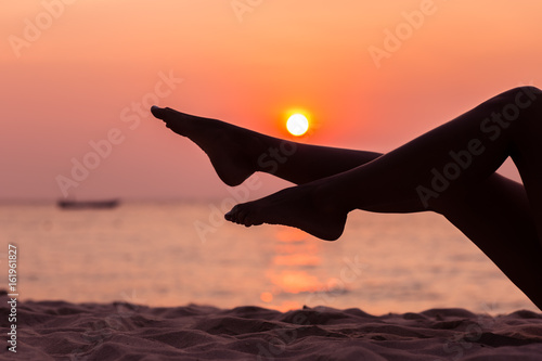 Female legs silhouette on sunset sea background, side view, back lit