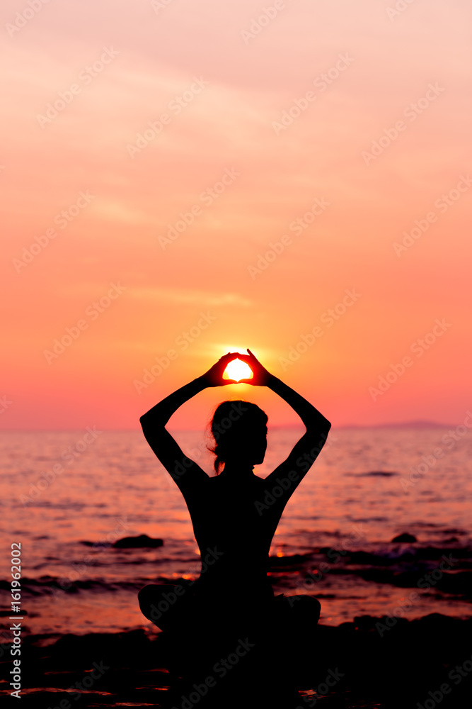 Woman silhouette sitting in lotus position on sunset sea background back lit
