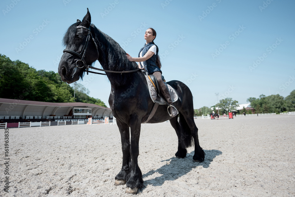 Confident young woman riding brown purebred horse Confident young woman riding brown purebred horse