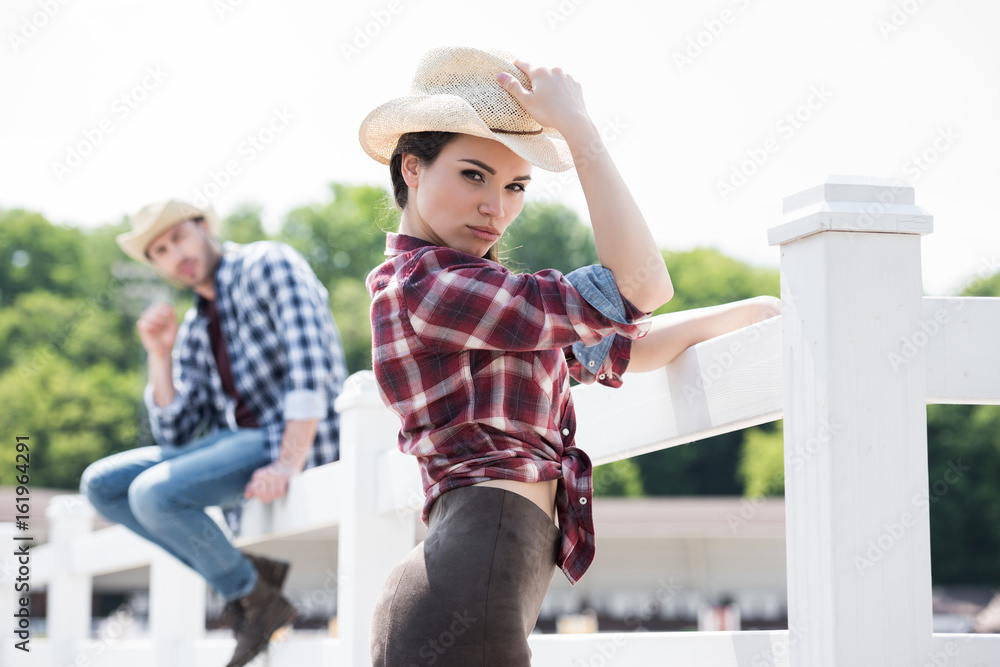 cowboy style girl posing and looking at camera near fence on ranch
