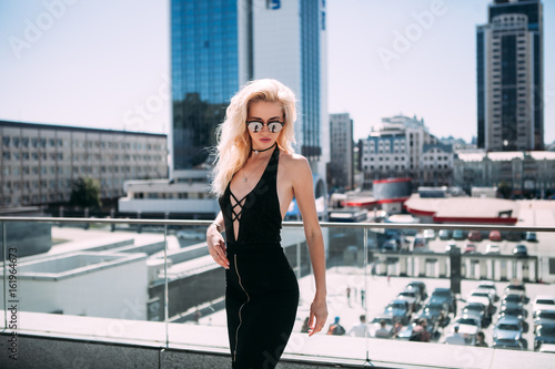 Female fashion concept. Outdoor waist up portrait of young beautiful woman posing on old street. Model wearing stylish clothes, looking at camera. Sunny day. City lifestyle.