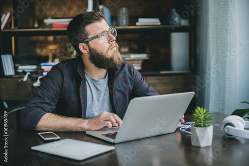 pensive bearded man typing on laptop while sitting at home