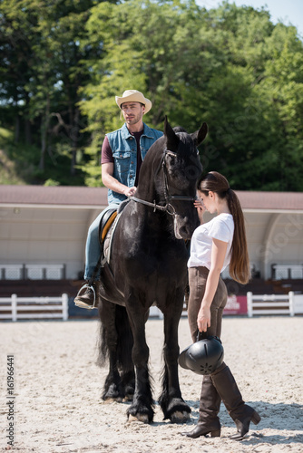 young man in cowboy hat sitting on horseback while woman stroking horse