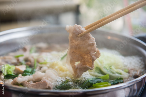 Shabu Shabu or Sukiyaki or hot pot  ,Hand holding pork using chopsticks, Japanese food in restaurant .