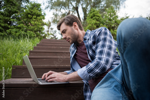 handsome casual man using laptop while sitting on stairs outdoors