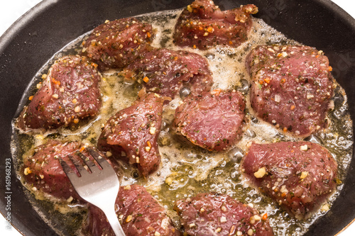 Smażenie mięsa na patelni. Mięso w przyprawach smażone w sosie. Mięso na patelni i widelec.