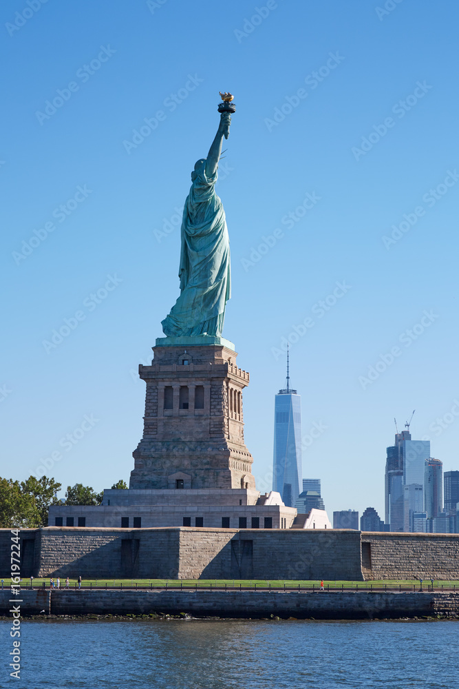Fototapeta premium Statue of Liberty island and New York city skyline in a sunny day, blue sky