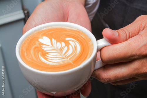 Barista holding cup latte art coffee in cafe.