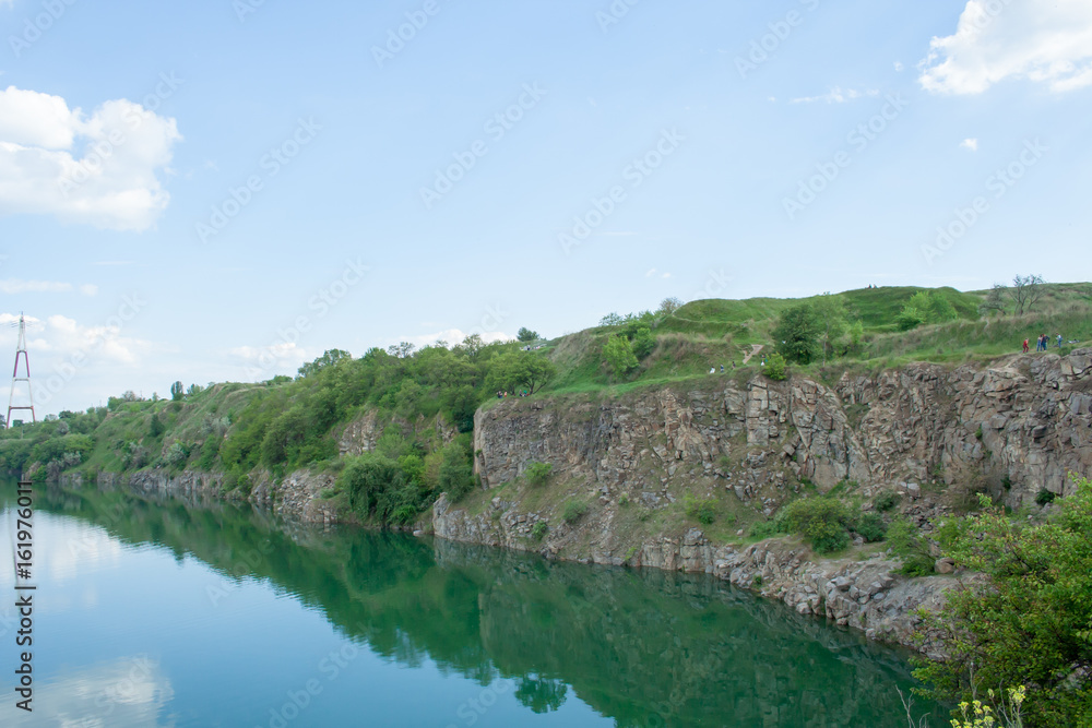 High rock on the shore of the lake, grass, gravel and dirt, sunny summer day