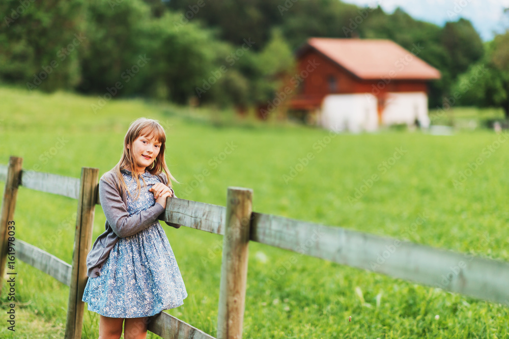 Naklejka premium Pretty kid girl playing in a beautiful summer park at sunset, resting on a fence, happy childhood in countryside
