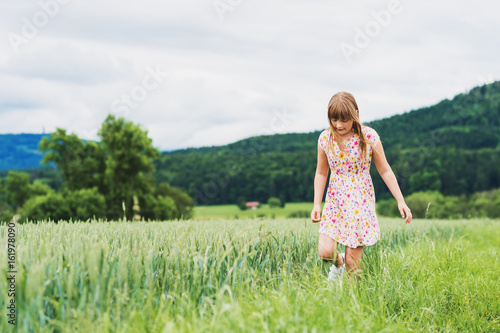 Fototapeta Naklejka Na Ścianę i Meble -  Little girl playing in green wheat field in summertime, wearing a dress
