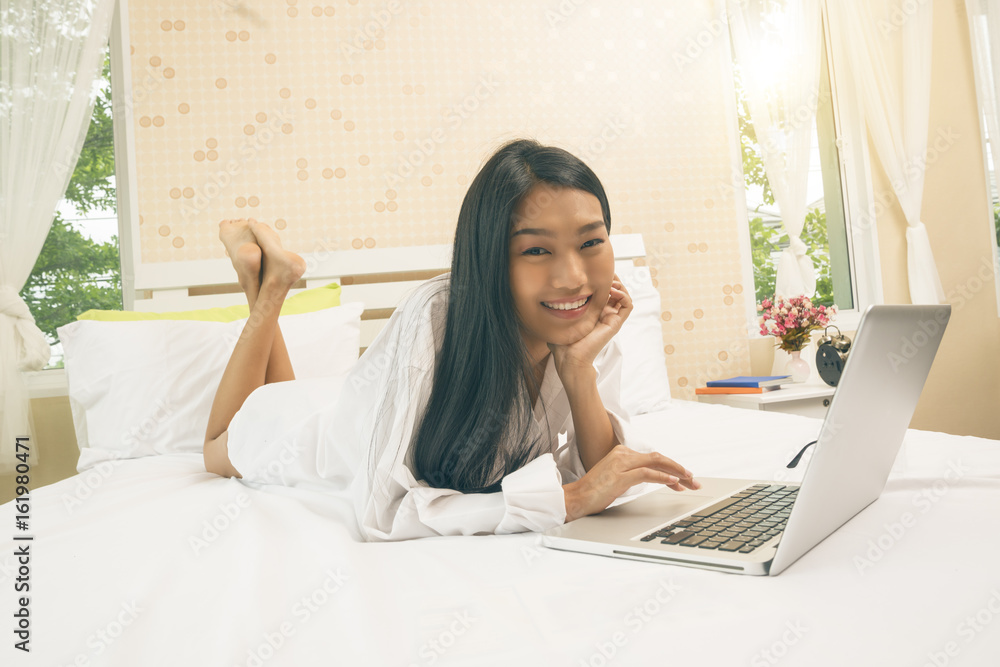Young asian woman with laptop watching a movie or working or shopping on line on notebook on the bed. Young asian woman with laptop watching a movie or working or shopping on line on notebook on the bed.