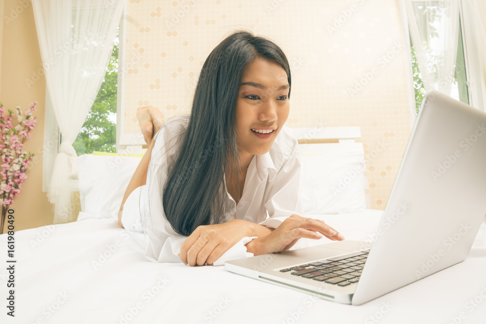 Young asian woman with laptop watching a movie or working or shopping on line on notebook on the bed. Young asian woman with laptop watching a movie or working or shopping on line on notebook on the bed.