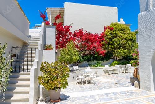 Typical Greek restaurant terrace with white tables and chairs and red summer flowers in Agia Anna. Naxos Island. Greece.