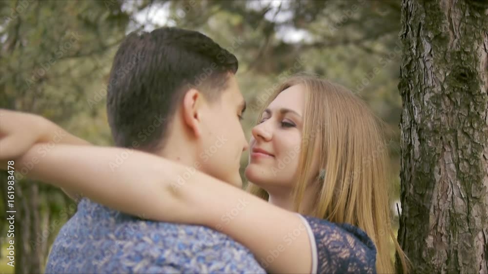 A beautiful young couple in love stroll, kiss and hug in a summer park near coniferous trees A beautiful young couple in love stroll, kiss and hug in a summer park near coniferous trees