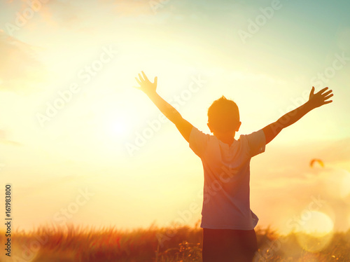 Little boy raising hands over sunset sky, enjoying life and nature