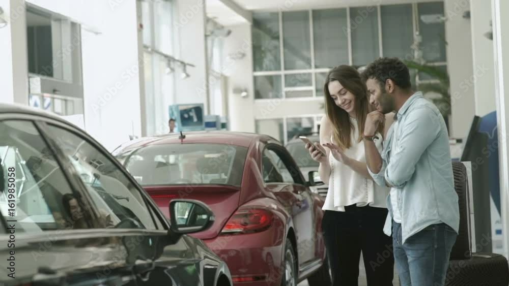 Swarht guy and beautiful girl uses the smartphone in car showroom Swarht guy and beautiful girl uses the smartphone in car showroom