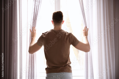 Young man opening curtains