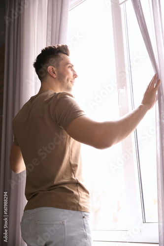 Young man opening curtains