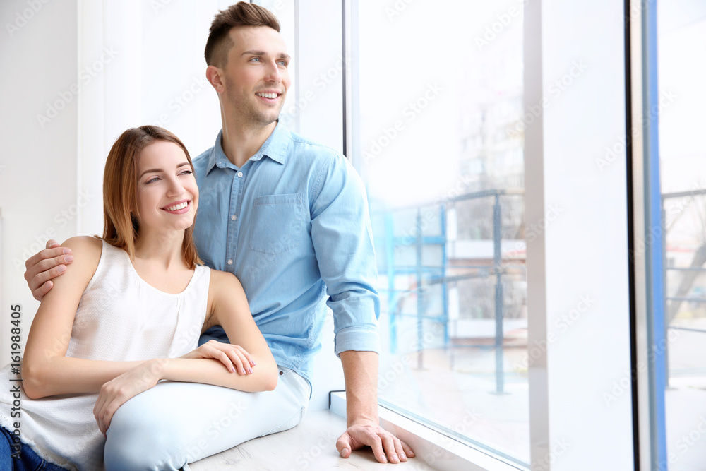 Happy couple sitting on sill near big white window