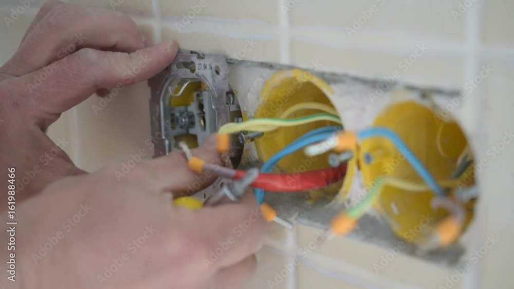 Electrician hands installing a wired electric plug into a wall and ...