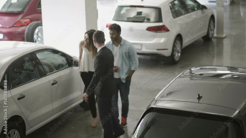 The manager of car showroom demonstrates the automobiles to young couple The manager of car showroom demonstrates the automobiles to young couple