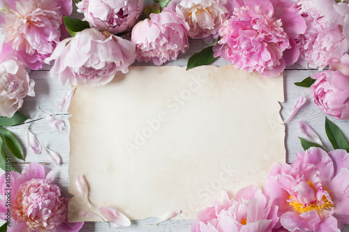 Pink peonies on a white wooden background and a paper blank for greeting text