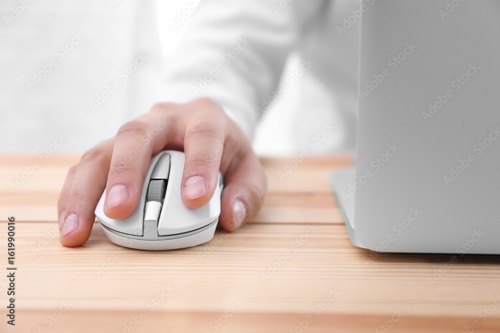 Male hand with computer mouse and laptop on table Male hand with computer mouse and laptop on table