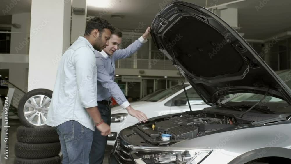 The manager demonstrates the customer a motor in modern car The manager demonstrates the customer a motor in modern car