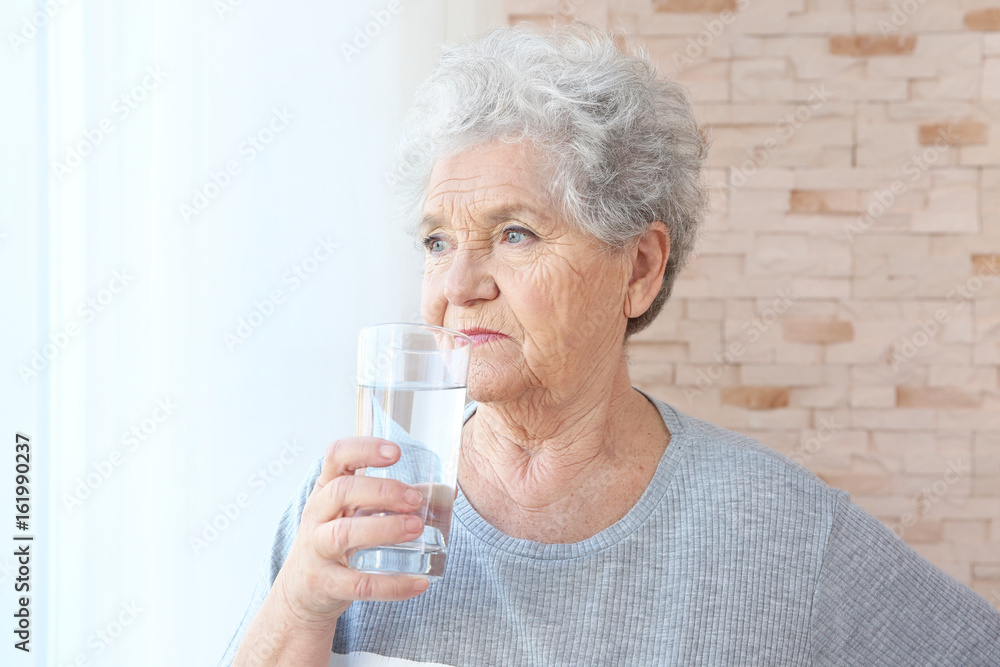 Elderly woman holding glass of water at home. Concept of retirement Elderly woman holding glass of water at home. Concept of retirement