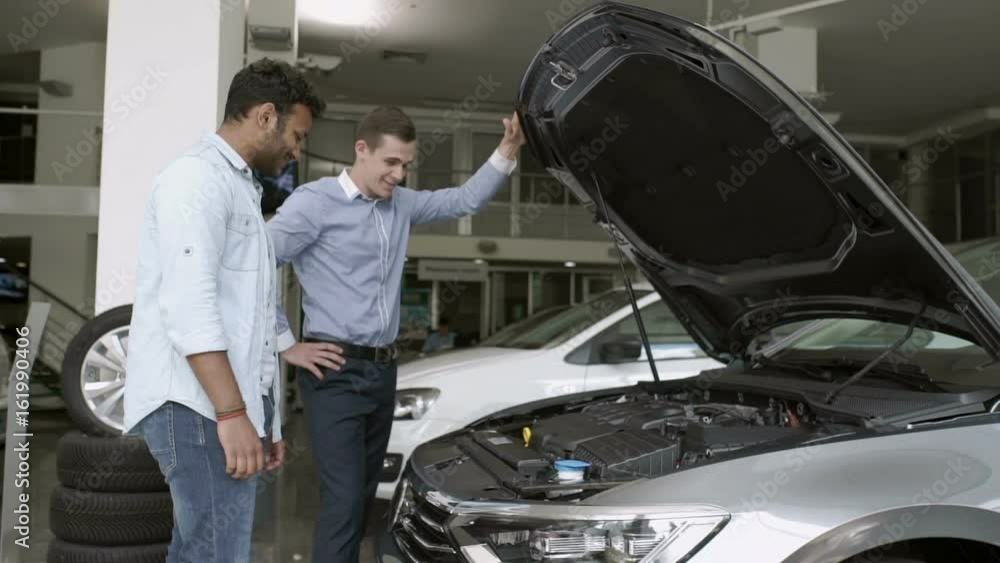 Salesman and buyer talks about motor of car in car showroom Salesman and buyer talks about motor of car in car showroom