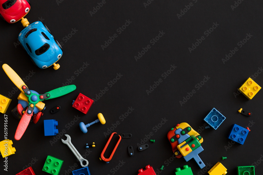 Colorful plastic bricks, cars and details of toys on black paper background. Parts of bright small spare parts for toys.
