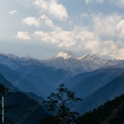 Kangchenjunga mountain with clouds above. Among green hills and trees that view in the evening in North Sikkim, India.