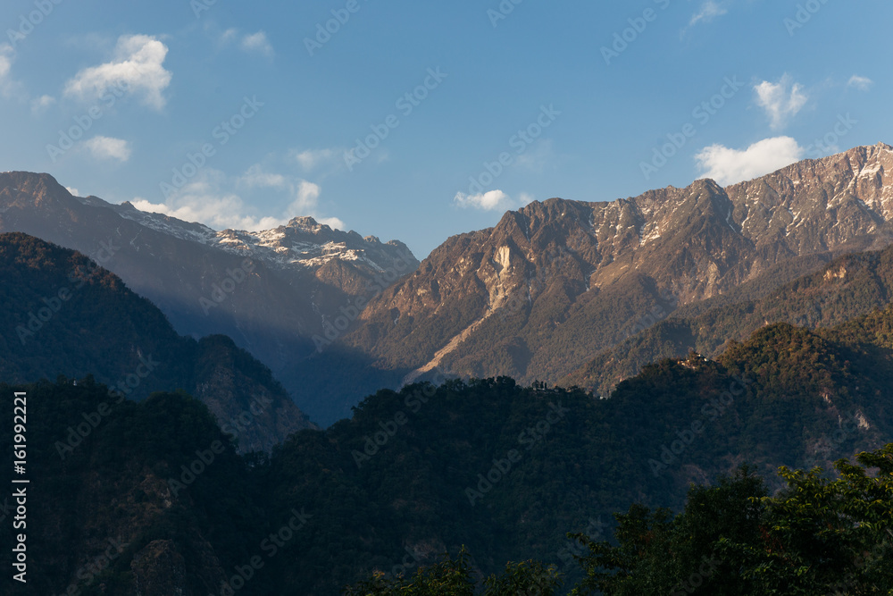 Green hill near Kangchenjunga mountain with clouds above and trees with sunlight that view in the evening in North Sikkim, India.