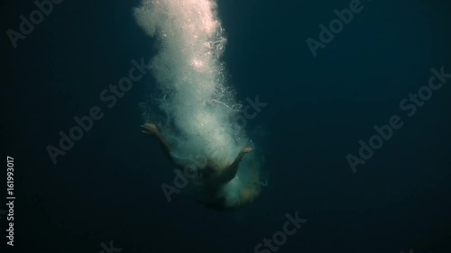 Young and beautiful girl is ducking under the water and beautifully falls to the bottom among the bubbles and boats on the background