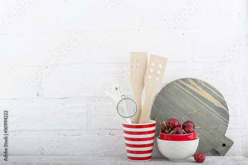 A simple kitchen still life against a white brick wall: cutting board, cooking equipment, ceramics. Horizontal photo