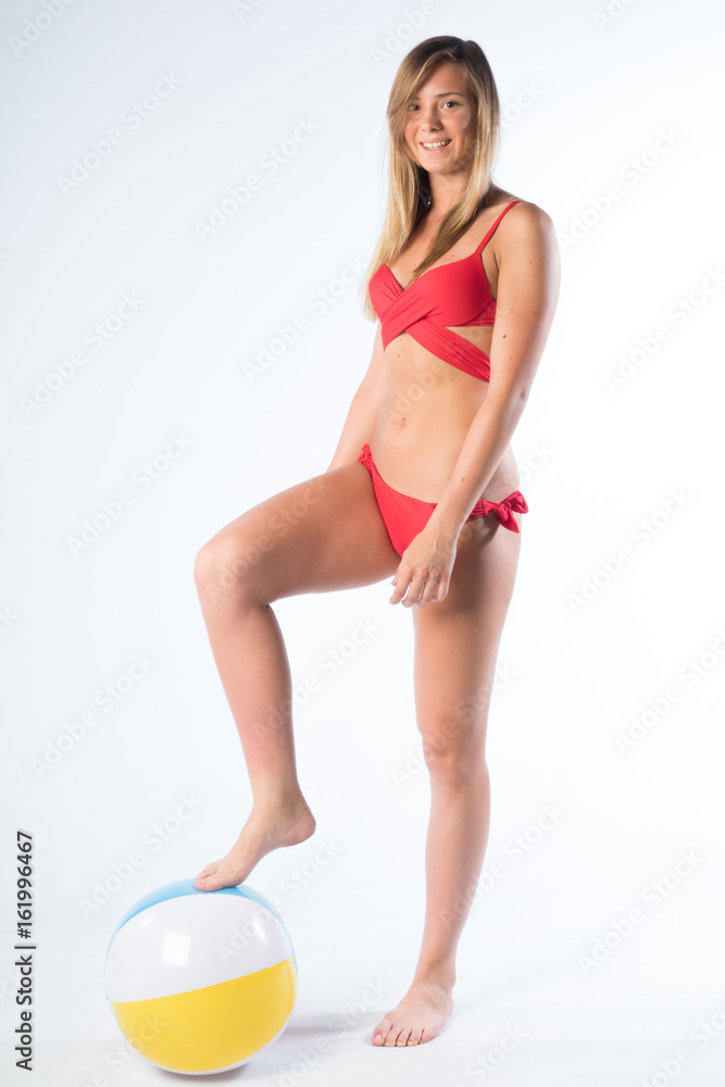 ragazza giovane in costume da bagno rosso con bellissimo fisico gioca con un pallone gonfiabile in studio su fondale bianco 