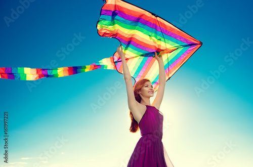 Beauty redhead girl with flying colorful kite over clear blue sky