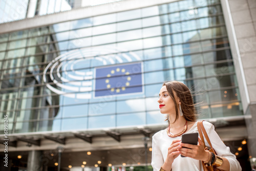 Fotografi Young businesswoman standing with phone near the Parliament building of European