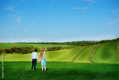 A young couple standing in the field, the girl shows her hand to the sky © cezarksv