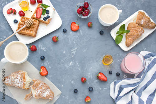 Breakfast concept frame with fresh berries waffles, croissant and coffee. Top view. Copy space