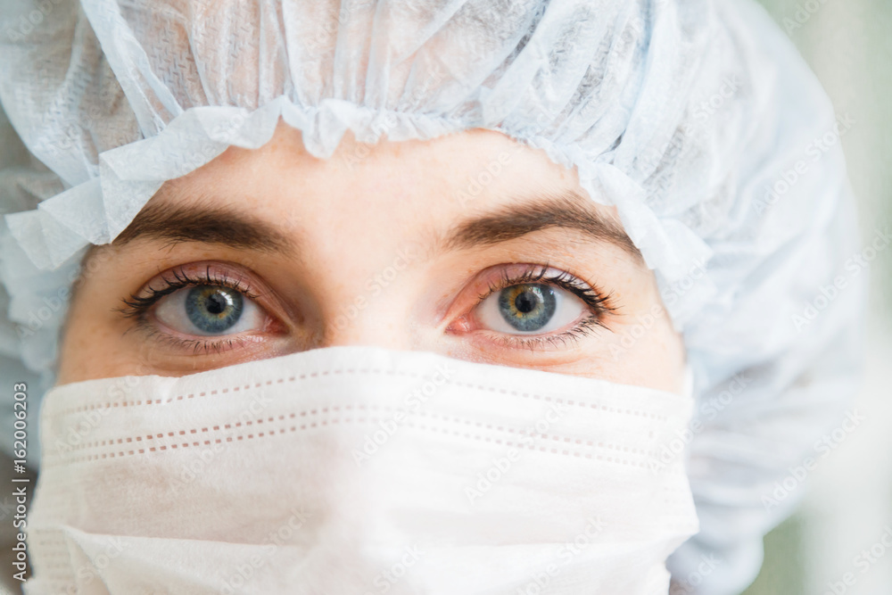 Close-up portrait of young female surgeon doctor or intern wearing protective mask and hat Close-up portrait of young female surgeon doctor or intern wearing protective mask and hat