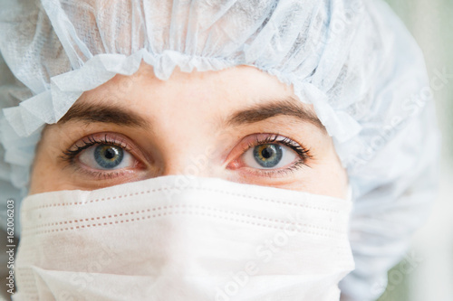 Close-up portrait of young female surgeon doctor or intern wearing protective mask and hat