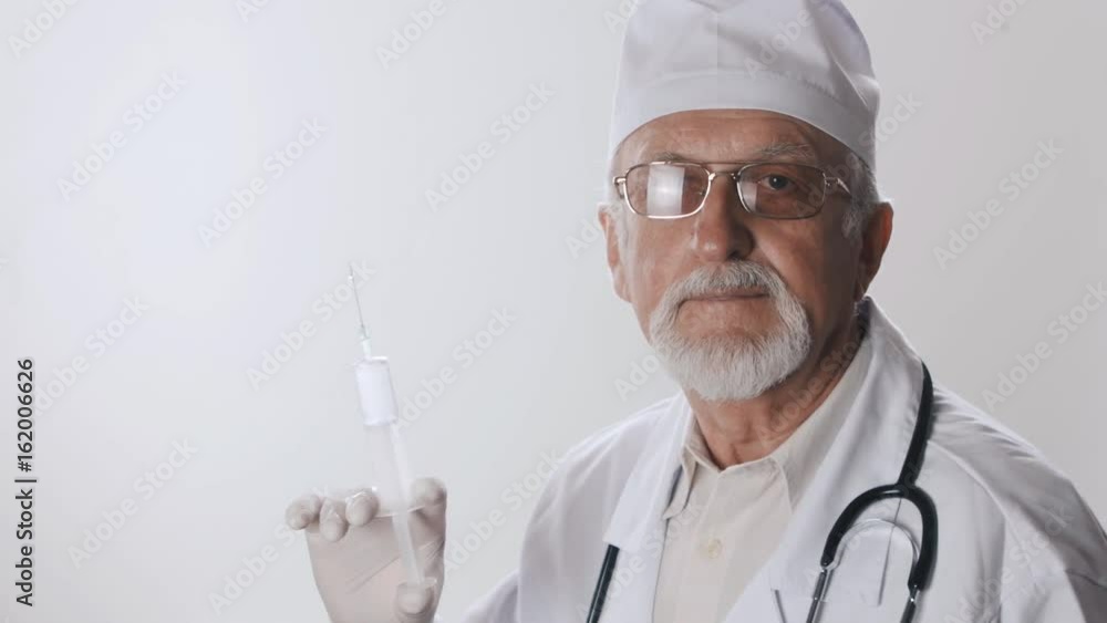 Portrait of an elderly doctor with a beard and glasses. Medical worker holds a syringe in his hands. Treatment with injections. Portrait of an elderly doctor with a beard and glasses. Medical worker holds a syringe in his hands. Treatment with injections.