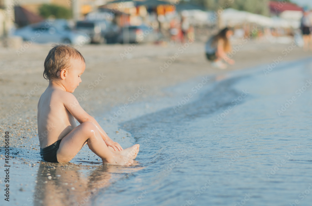 the child is seated near the sea, in the water, washes the feet of the child is seated near the sea, in the water, washes the feet of