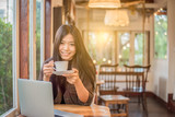 asian woman drinking coffee and looking something on laptop in the conner in  coffee shop