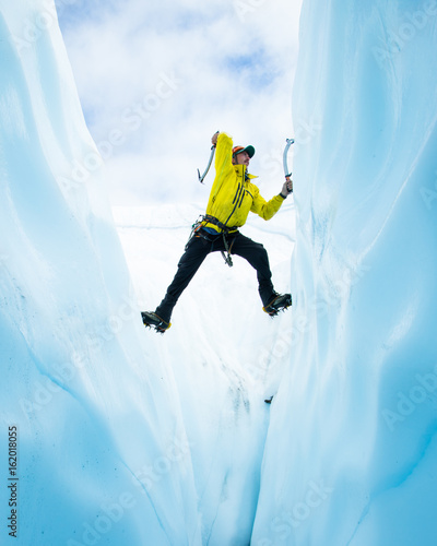Ice climber with no rope spanning a crevasse swinging an ice tool