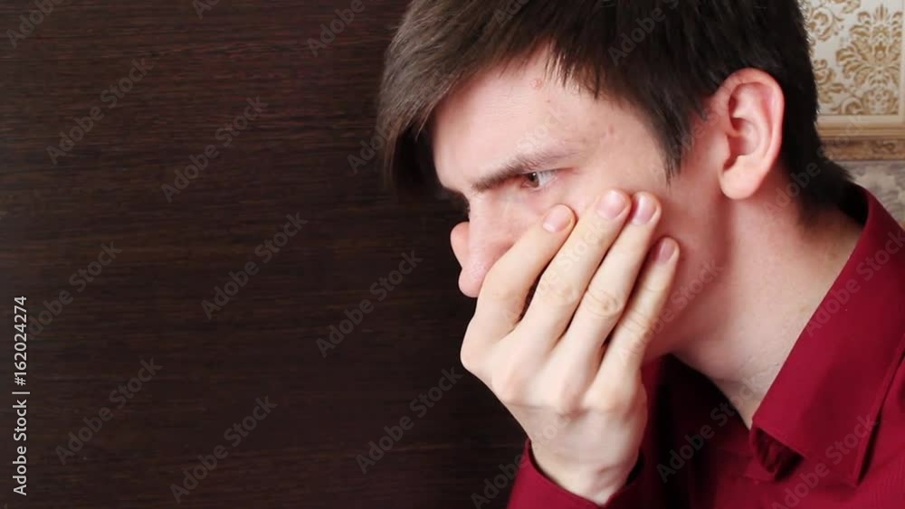 A young guy in a red shirt covered his mouth with his hand, looks closely A young guy in a red shirt covered his mouth with his hand, looks closely