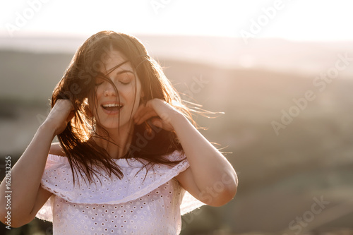 Beautiful girl remains on top of a mountain and looks at the horizon with a beautiful background. A colorful photo of a natural sunset  a miracle  incredible  a dance  hair in the wind